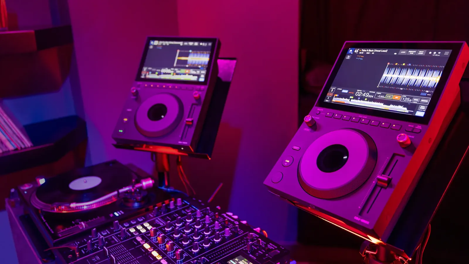 Dos AlphaTheta CDJ-1500X en una cabina con luz magenta, junto a un plato y una mesa de mezclas